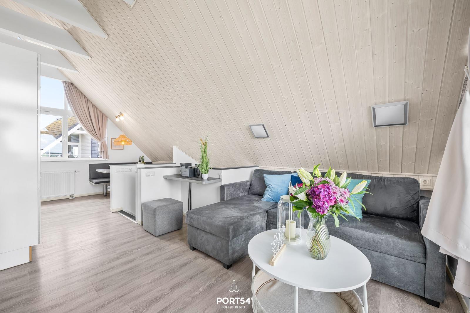Wohnbereich mit grauem Sofa, runden Tisch und Holzdecke