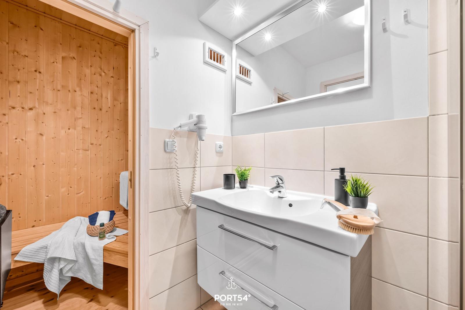 Bad mit Waschbecken, Spiegel und angrenzender Sauna.