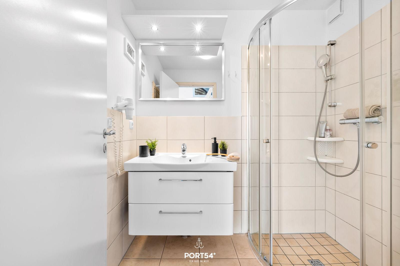 Badezimmer mit Dusche, Waschbecken und Spiegel.