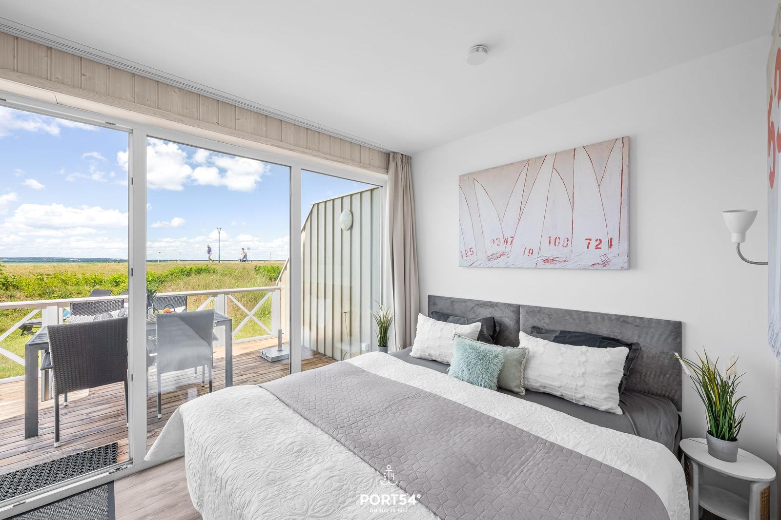 Schlafzimmer mit Balkon, Bett, Wandbild und Pflanzen.
