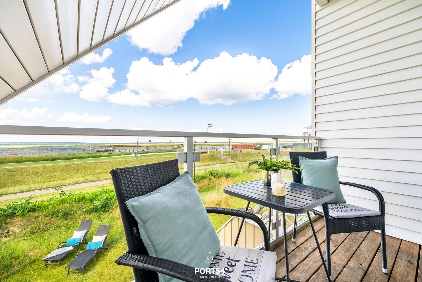 Terrasse mit Sitzgruppe und Blick auf Wasser und Grünfläche.