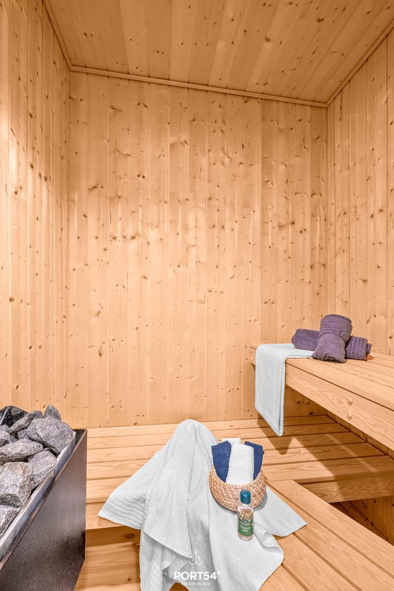 Sauna mit Holzwand, Sitzbänken, Handtuch und Steinbecken.