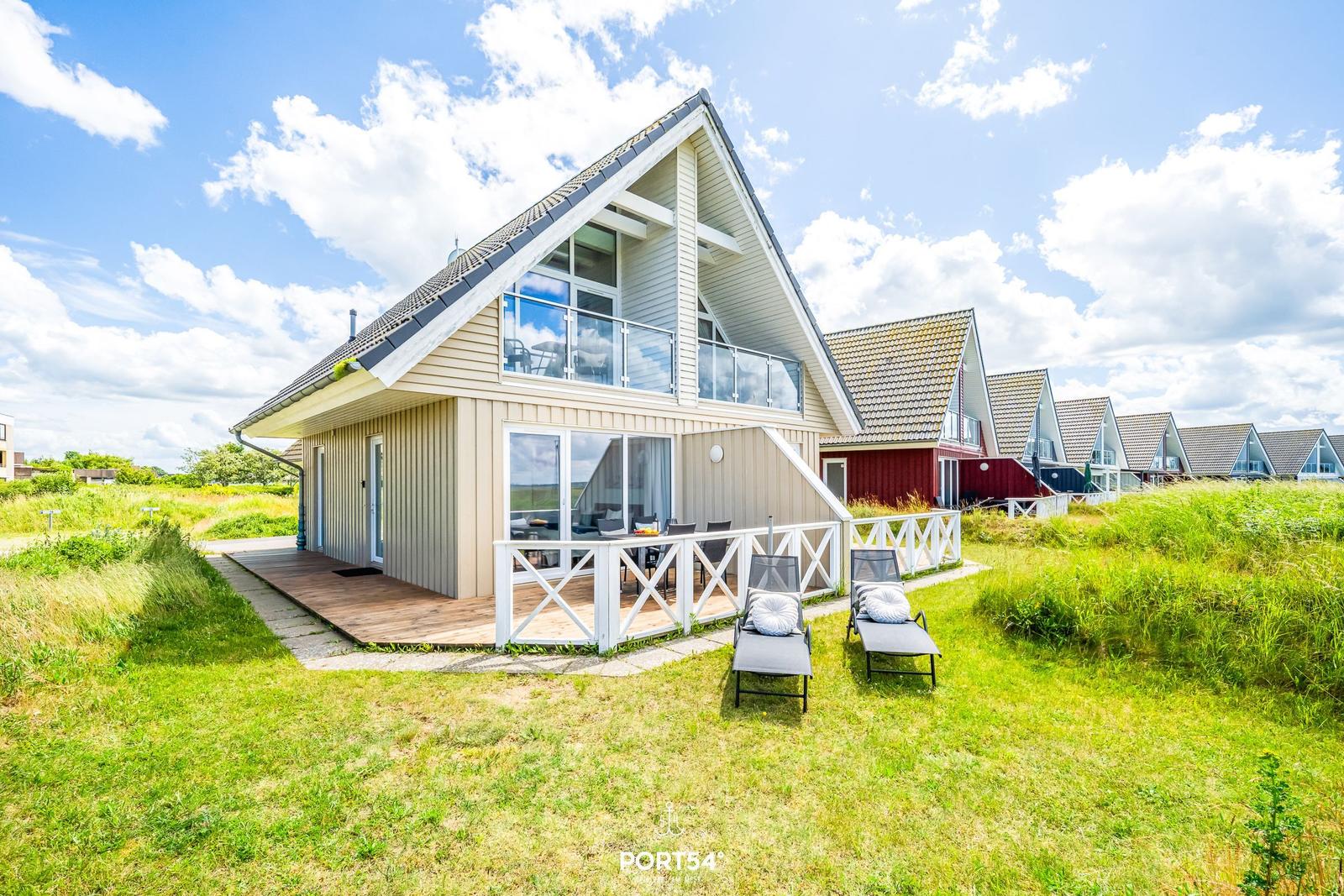 Moderne Ferienhaus mit Balkon, Terrasse und Liegestühlen auf grünem Grund.
