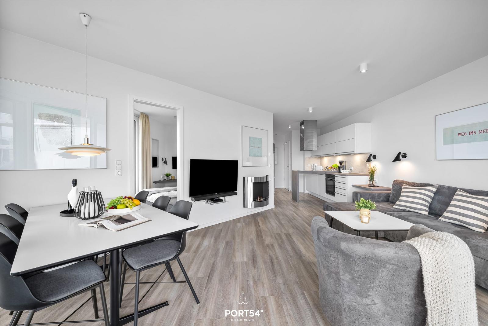 Wohnküche mit Esstisch, Sofa und Fernseher. Holzboden und weiße Wände.