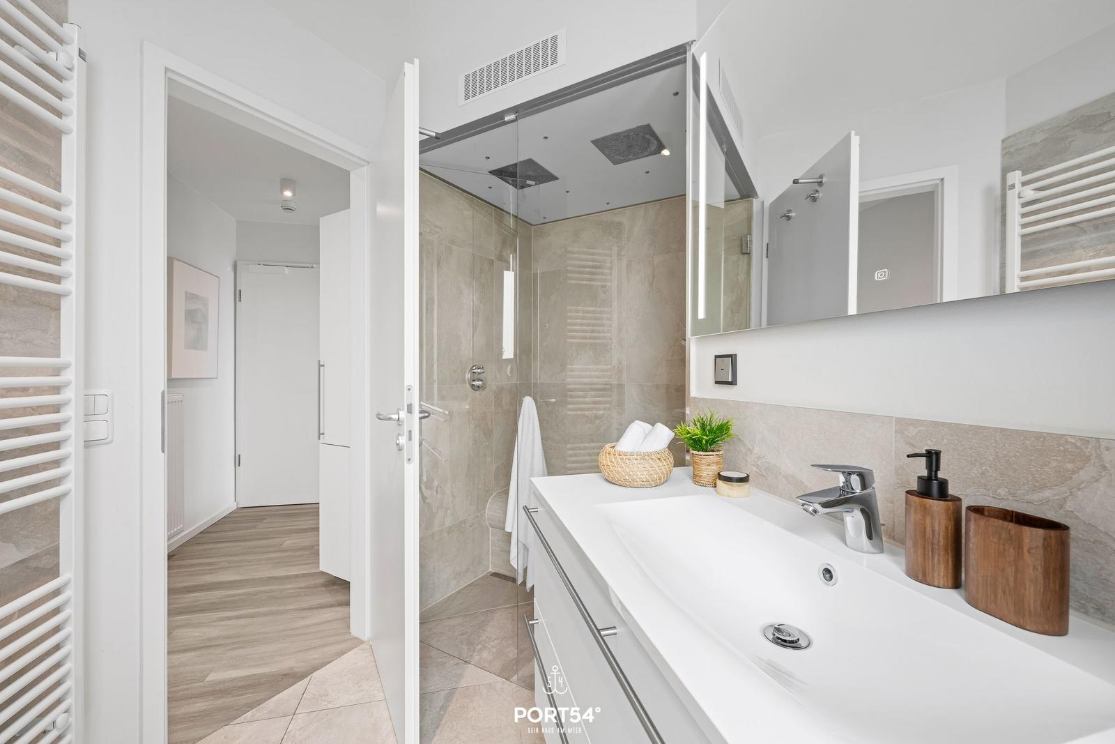 Badezimmer mit Dusche, Waschbecken und Spiegel. Holzfußboden und Heizung.