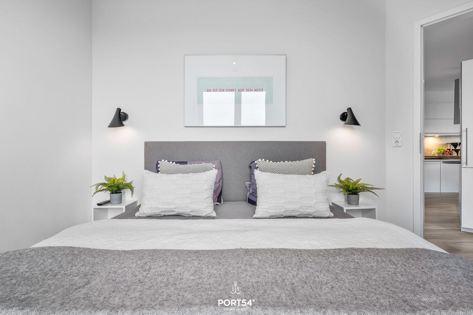 Schlafzimmer mit Doppelbett, Kopfteil, Nachttischen und Wandbild.