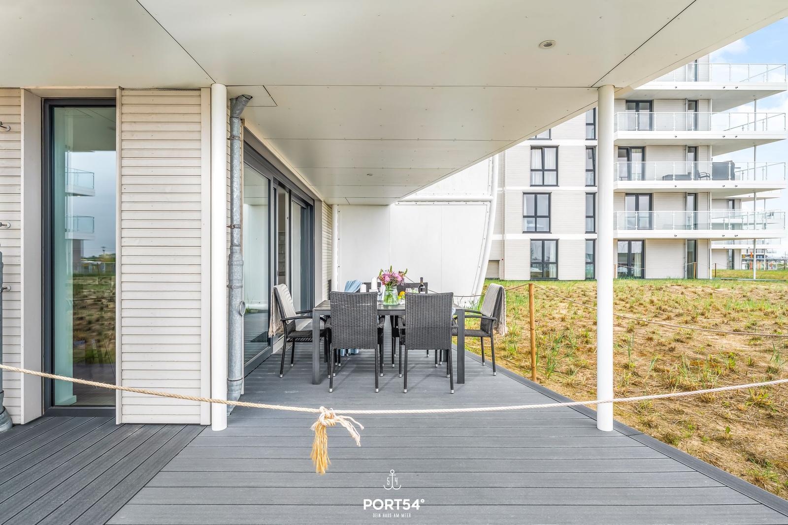 Terrasse mit Tisch und Stühlen unter Dach. Im Hintergrund Mehrfamilienhaus.
