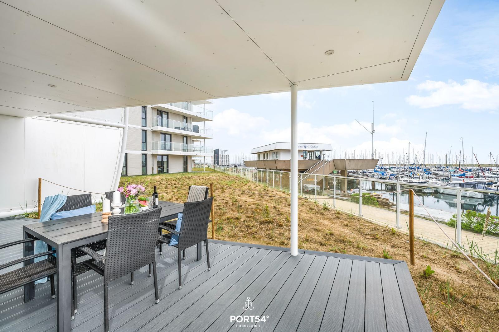 Terrasse mit Tisch und Stühlen, Blick auf Hafen mit Booten.