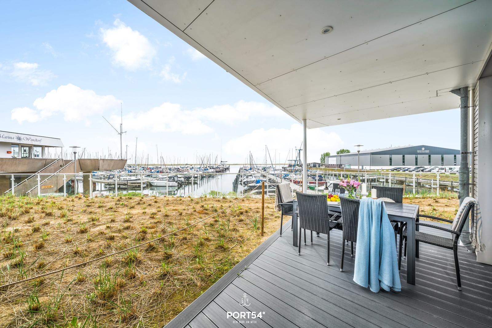 Terrasse mit Tisch und Stühlen bietet Blick auf Hafen mit Booten.