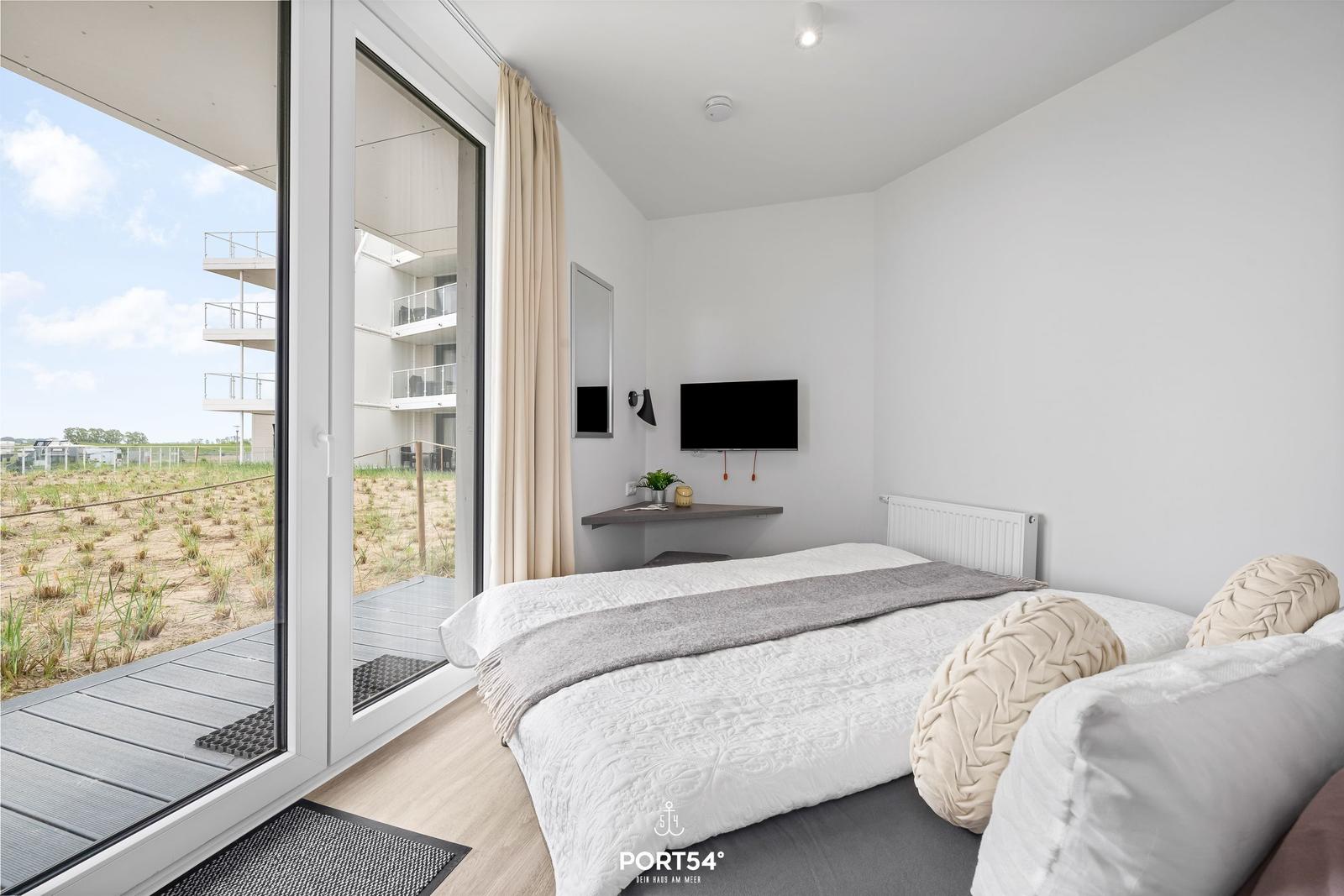 Schlafzimmer mit Bett, TV und Balkonansicht. Moderne Einrichtung mit neutralen Farben.