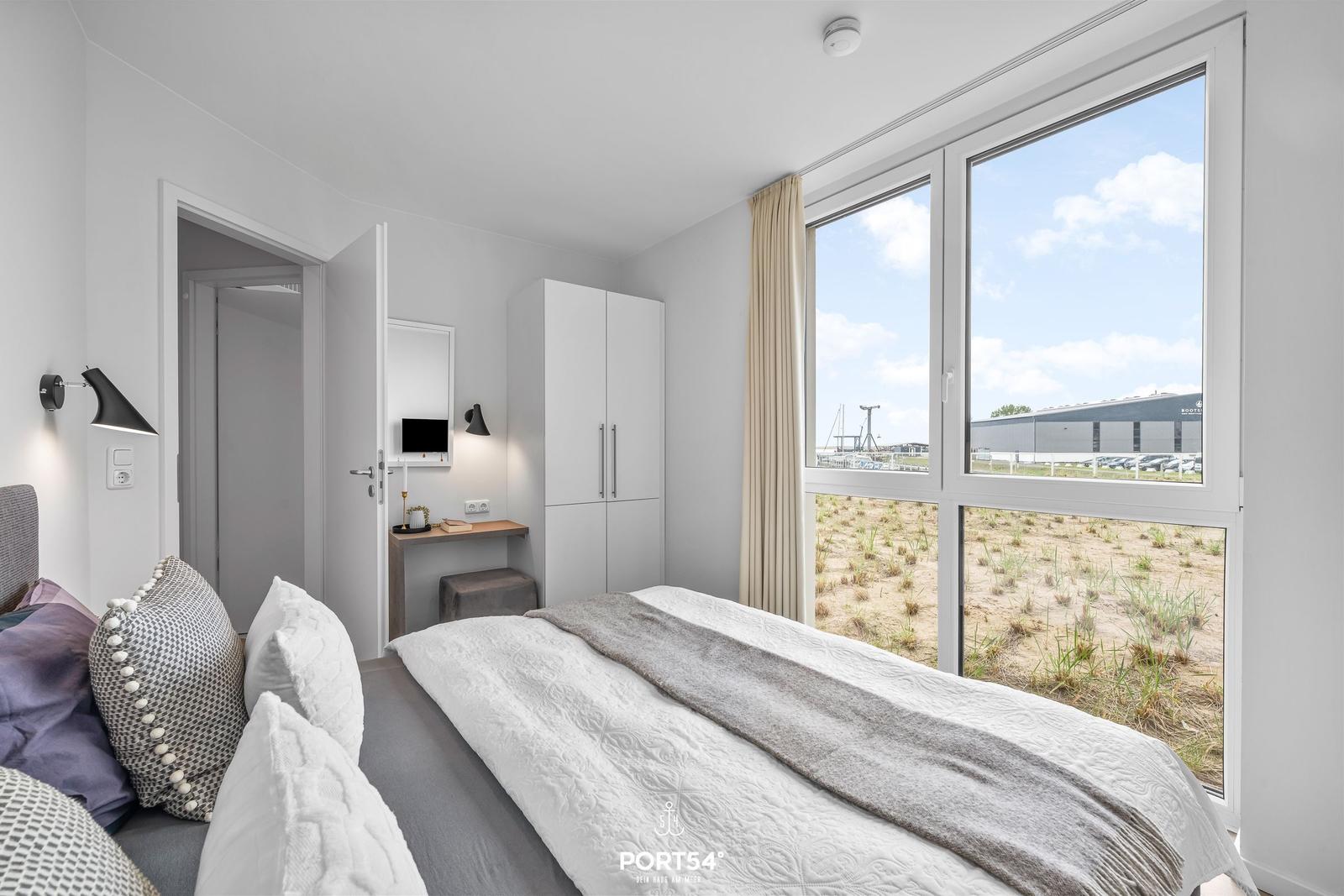 Schlafzimmer mit großem Fenster und Blick auf Hafenbereich.