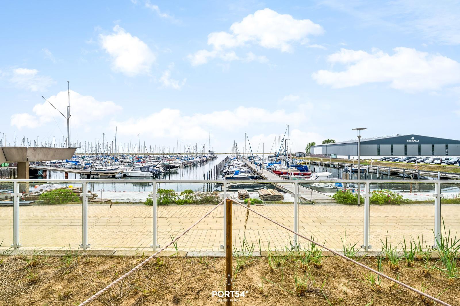 Hafen mit Booten und Steg unter blauem Himmel.
