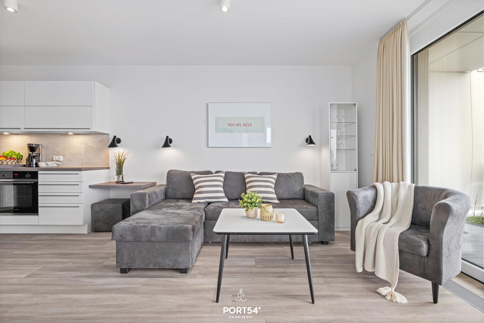 Wohnbereich mit grauem Sofa, Küchenzeile und Glasfront