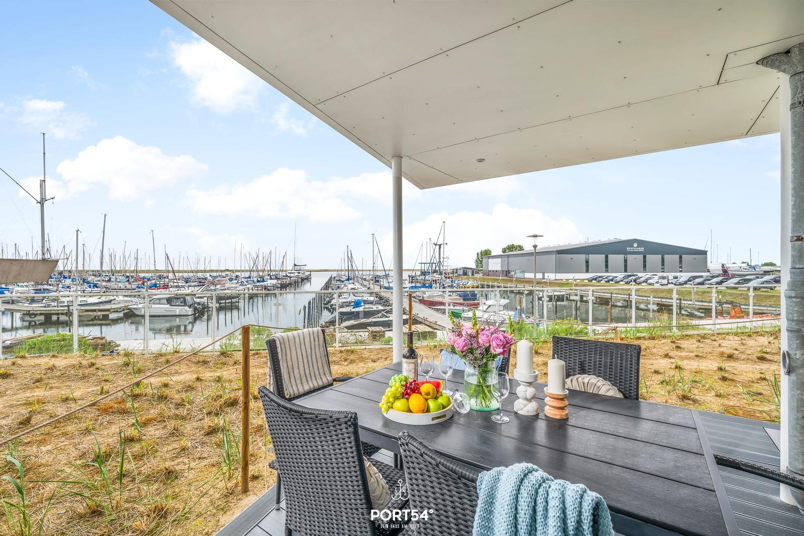 Terrasse mit Tisch und Stühlen, Blick auf Hafen mit Booten.