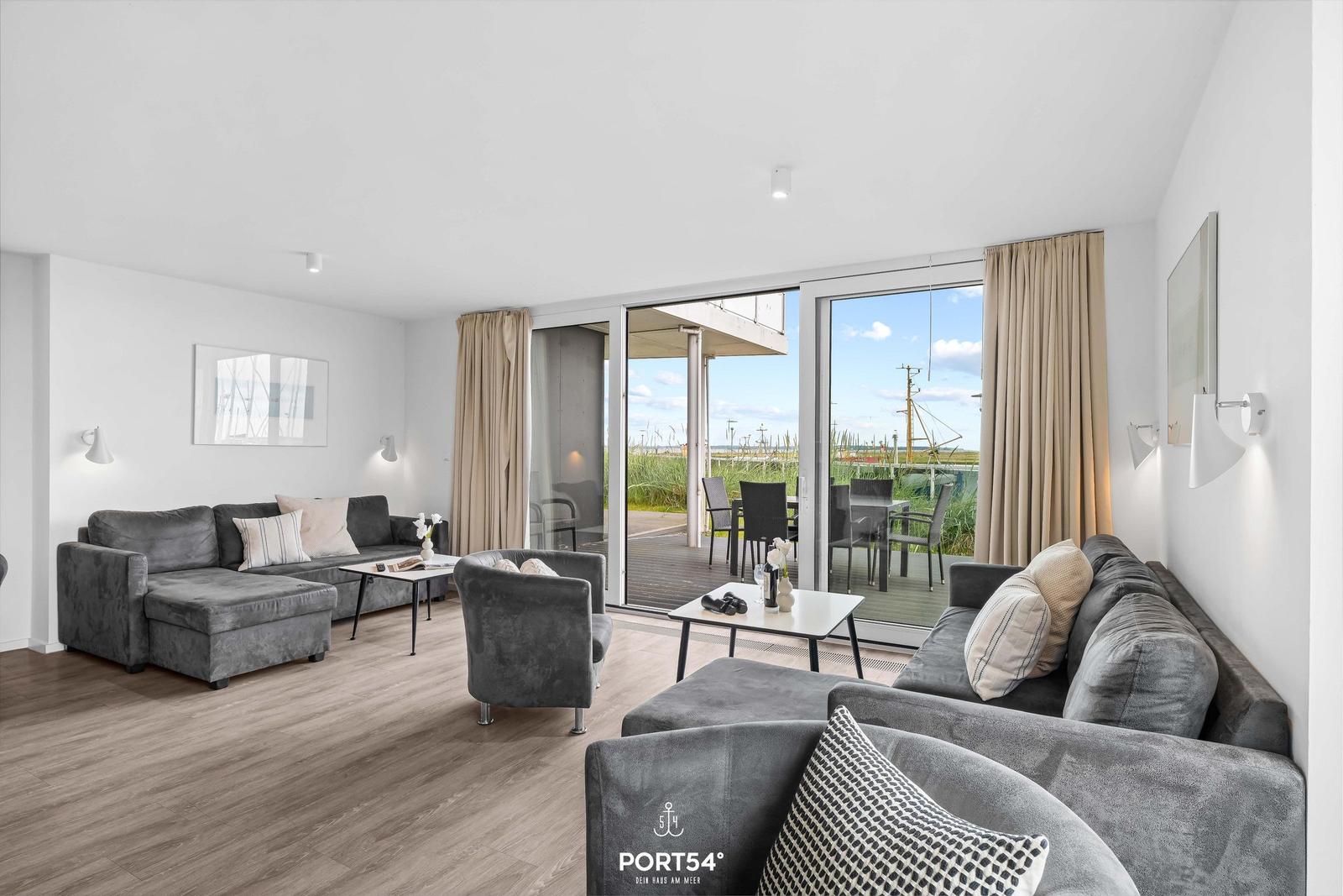 Wohnzimmer mit grauen Sofas, Holzboden und Blick auf Balkon mit Garten.