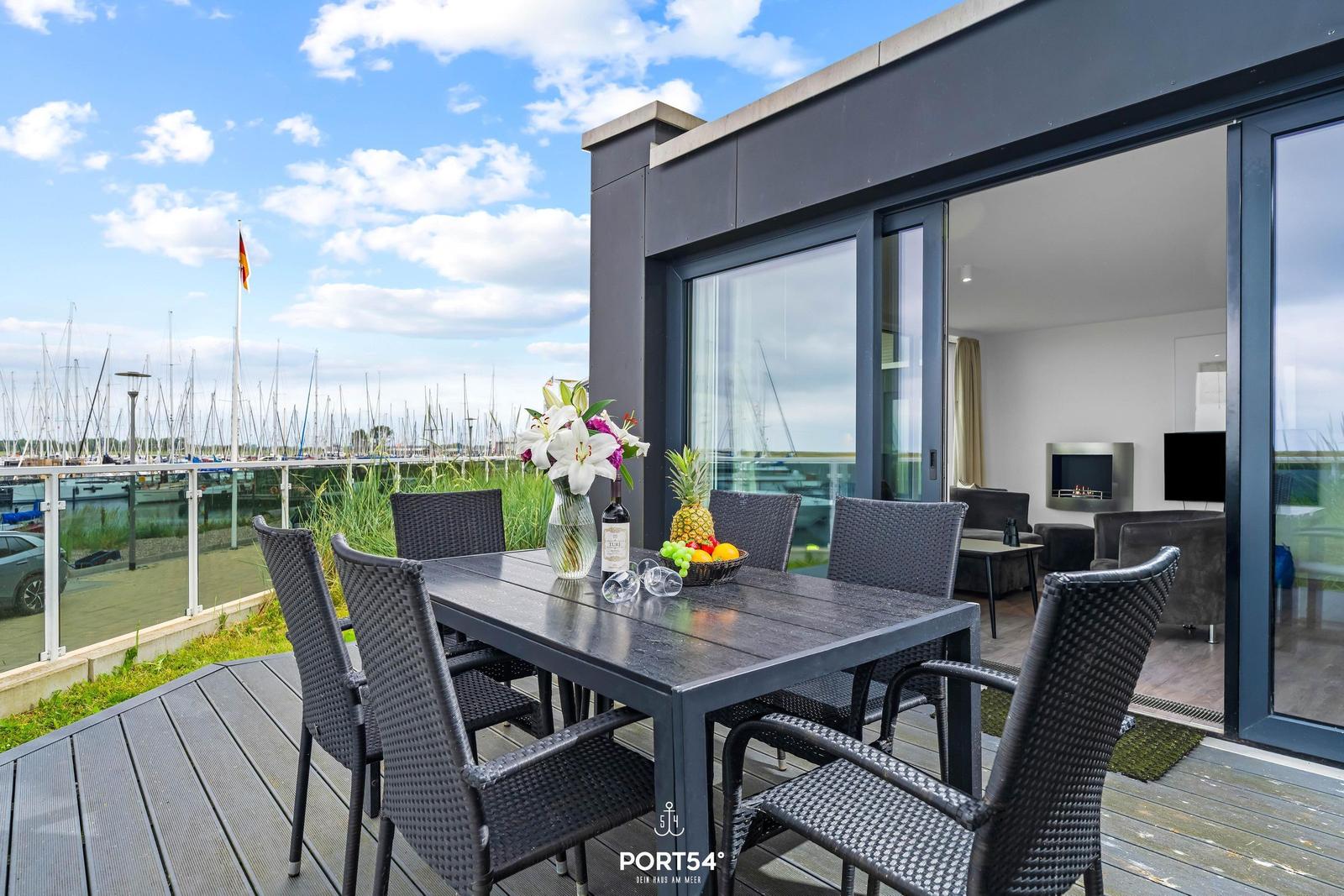 Terrasse mit Tisch und Stühlen, Blick auf Hafen mit Booten und Flagge.