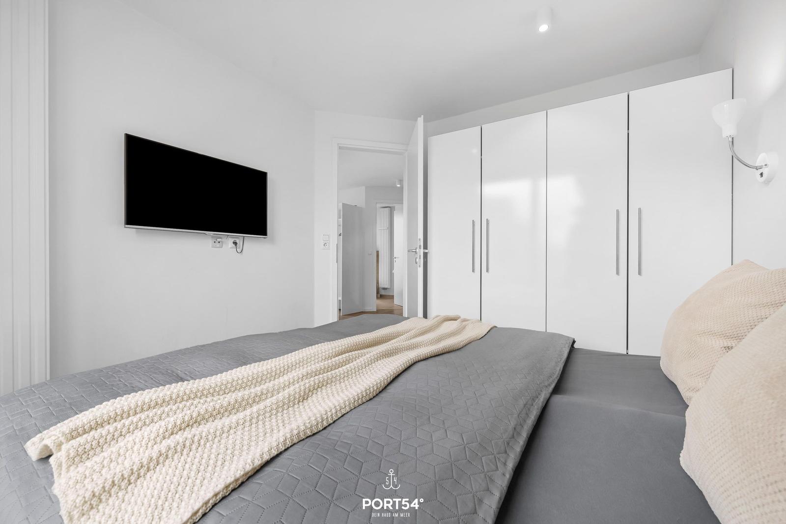Schlafzimmer mit Bett, Kleiderschrank und Wandfernseher.
