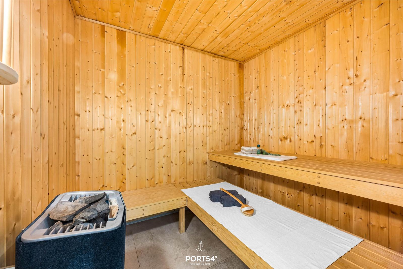 Sauna mit Holzwand, Bänken und Steinen. Handtuch und Bürste auf der Bank.