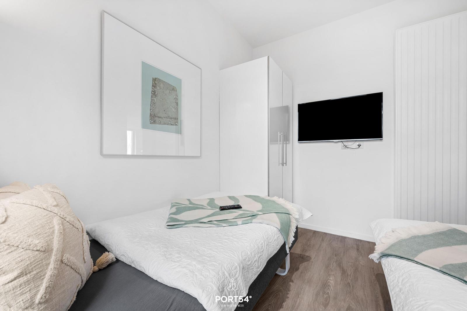 Zimmer mit zwei Betten, Fernseher und Kleiderschrank an der Wand.
