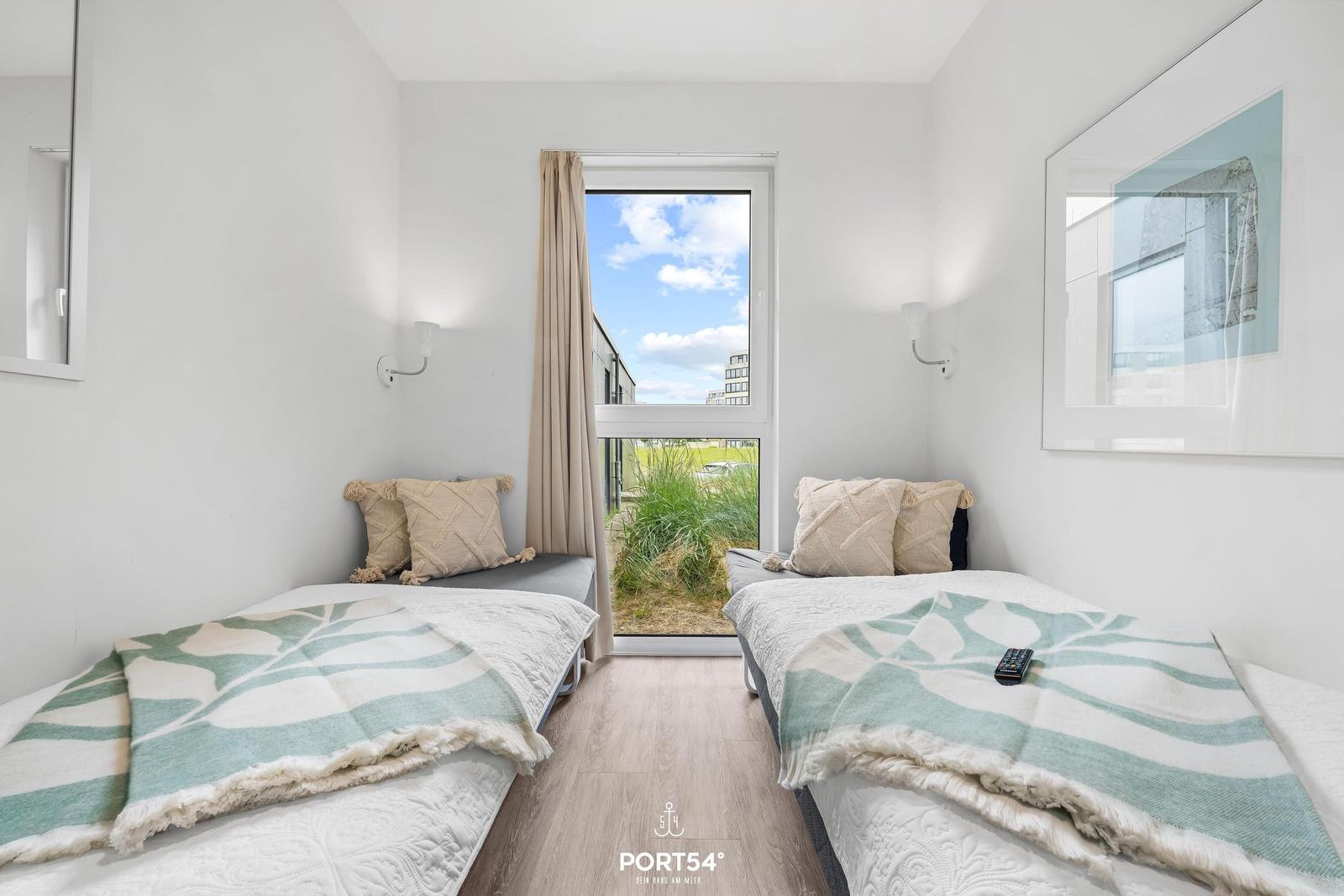 Zwei Betten mit Decken und Kissen. Fenster mit Blick auf Grünfläche.