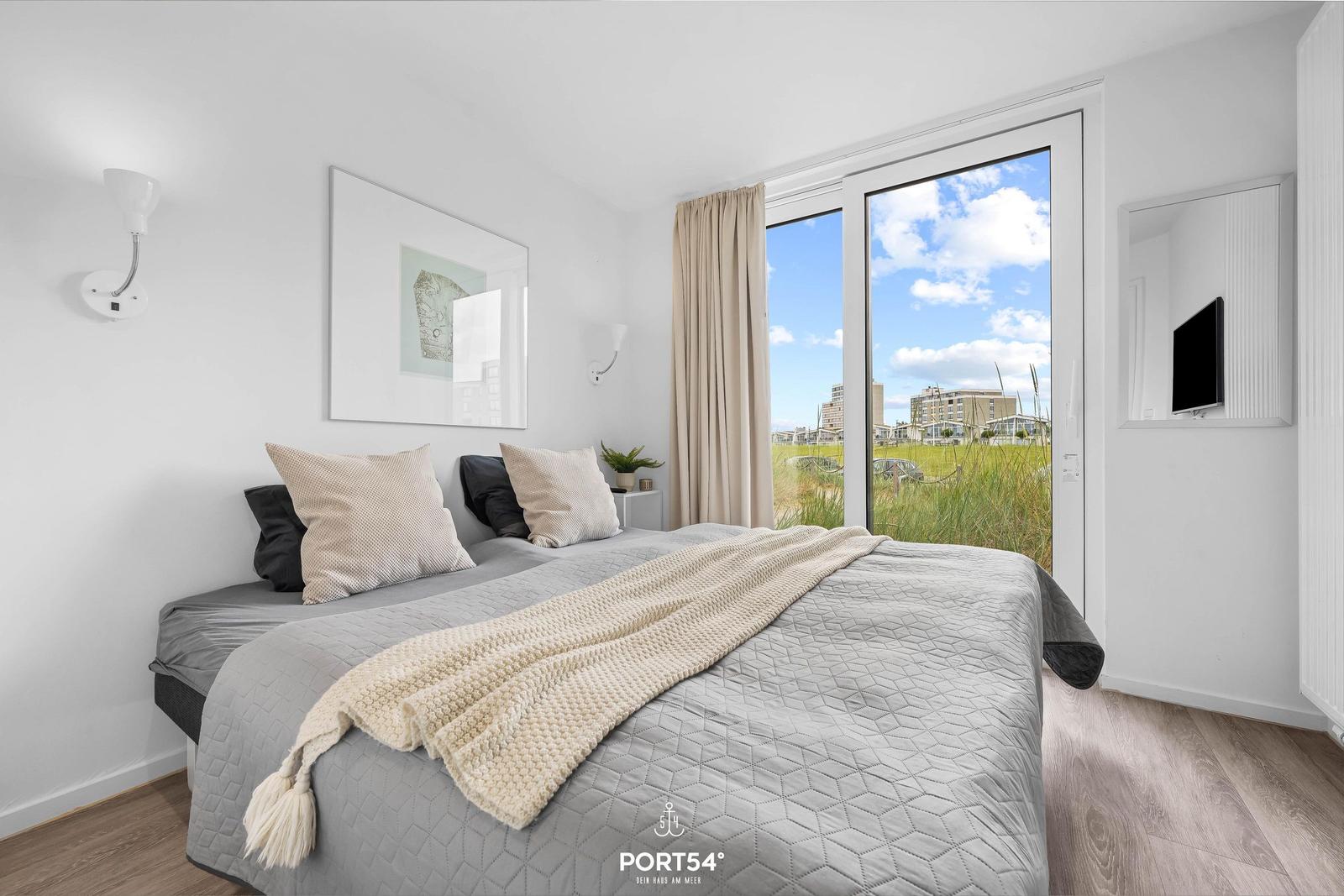 Schlafzimmer mit Doppelbett, Fenster und Fernseher.