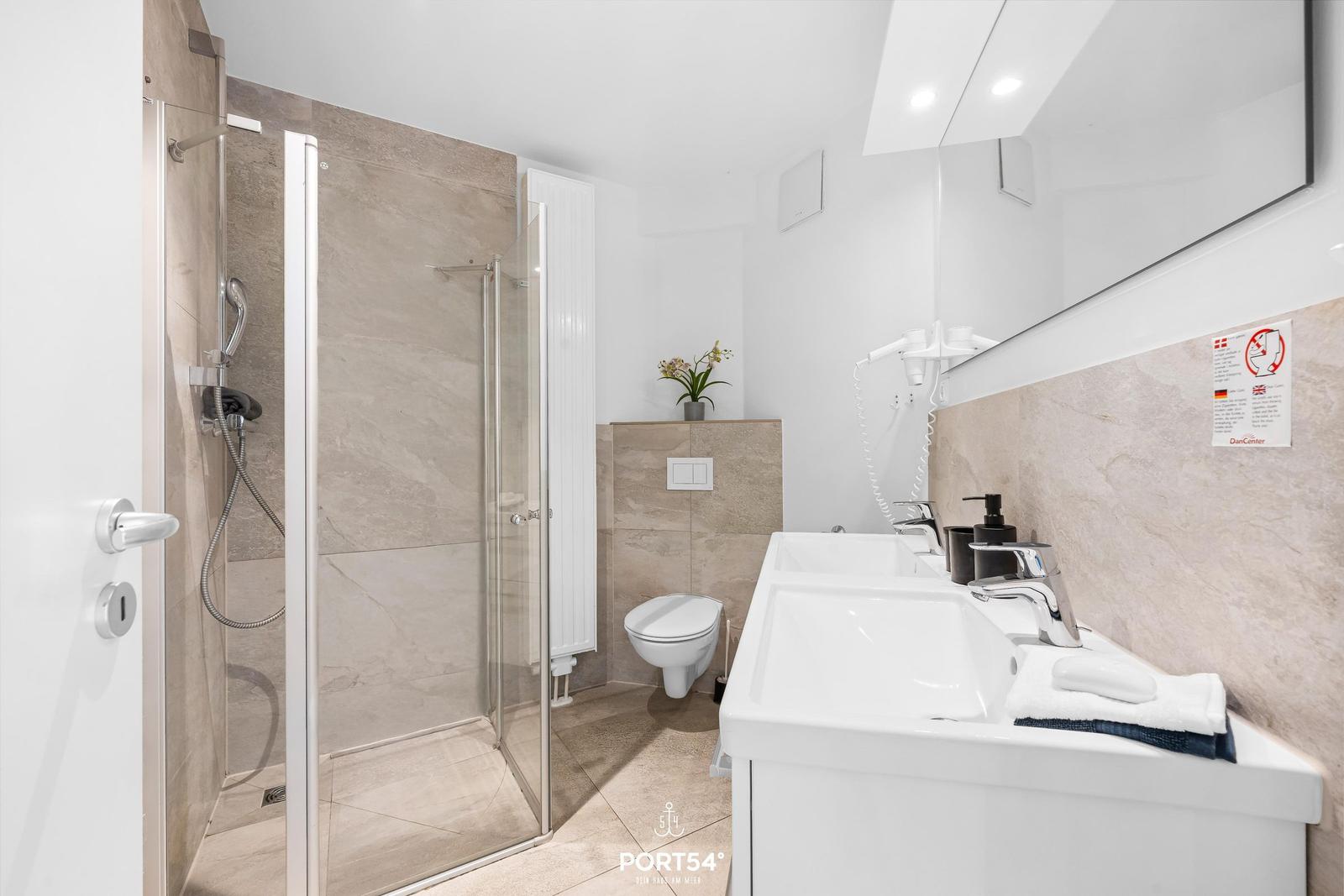 Badezimmer mit Dusche, Toilette und Waschbecken. Wandfliesen und Spiegel.