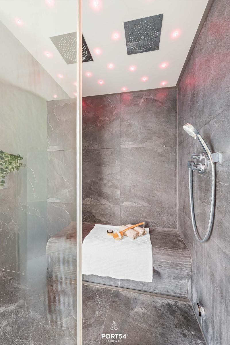 Dusche mit Duschsitz, Duschkopf und LED-Beleuchtung an der Decke.