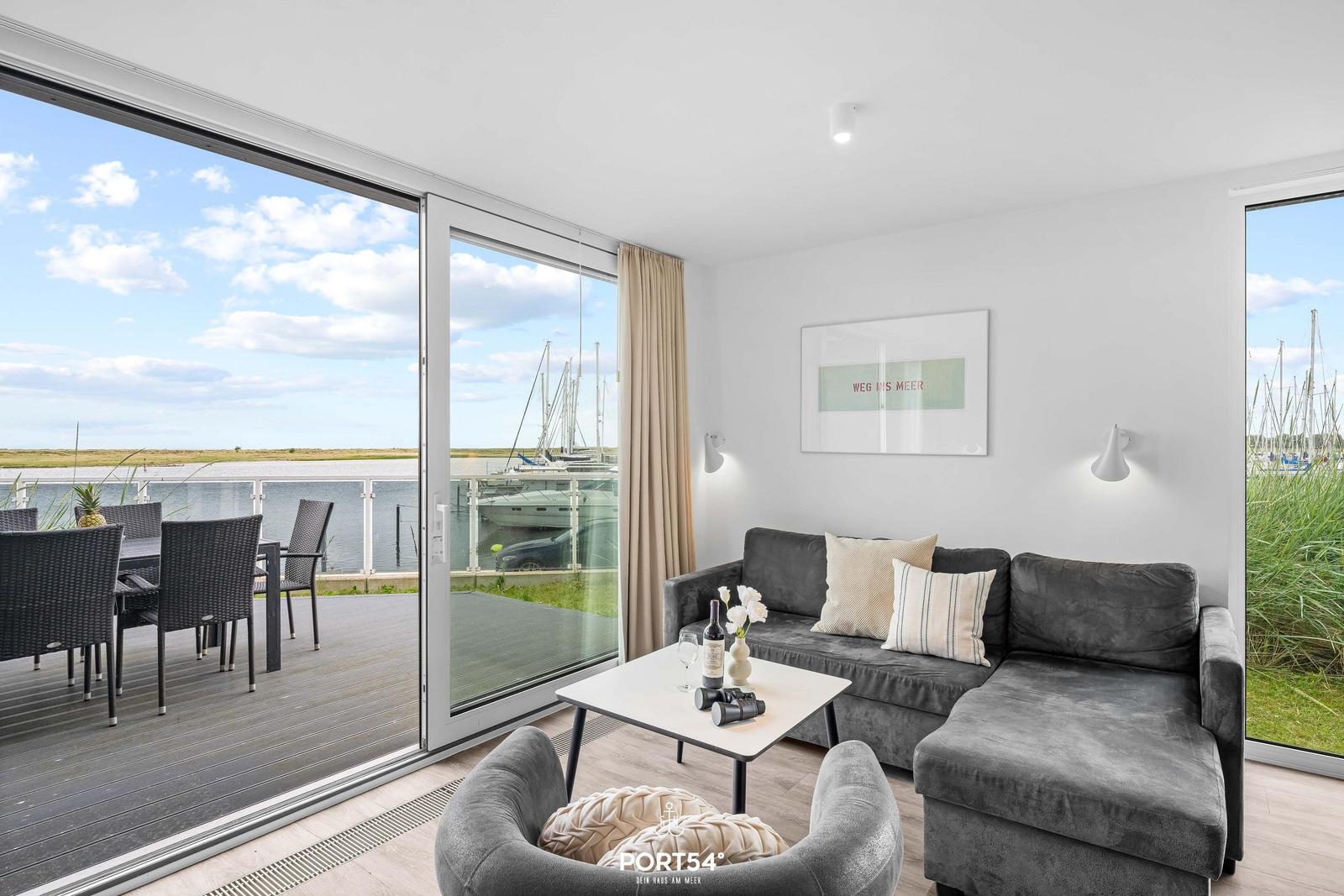 Wohnbereich mit Blick auf Hafen und Yachten. Sofa, Couchtisch und Terrasse.