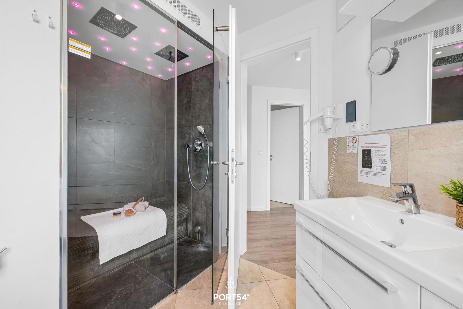 Dusche mit Regenduschkopf und LED-Beleuchtung, Waschbecken mit Spiegel und Handtuchhalter.