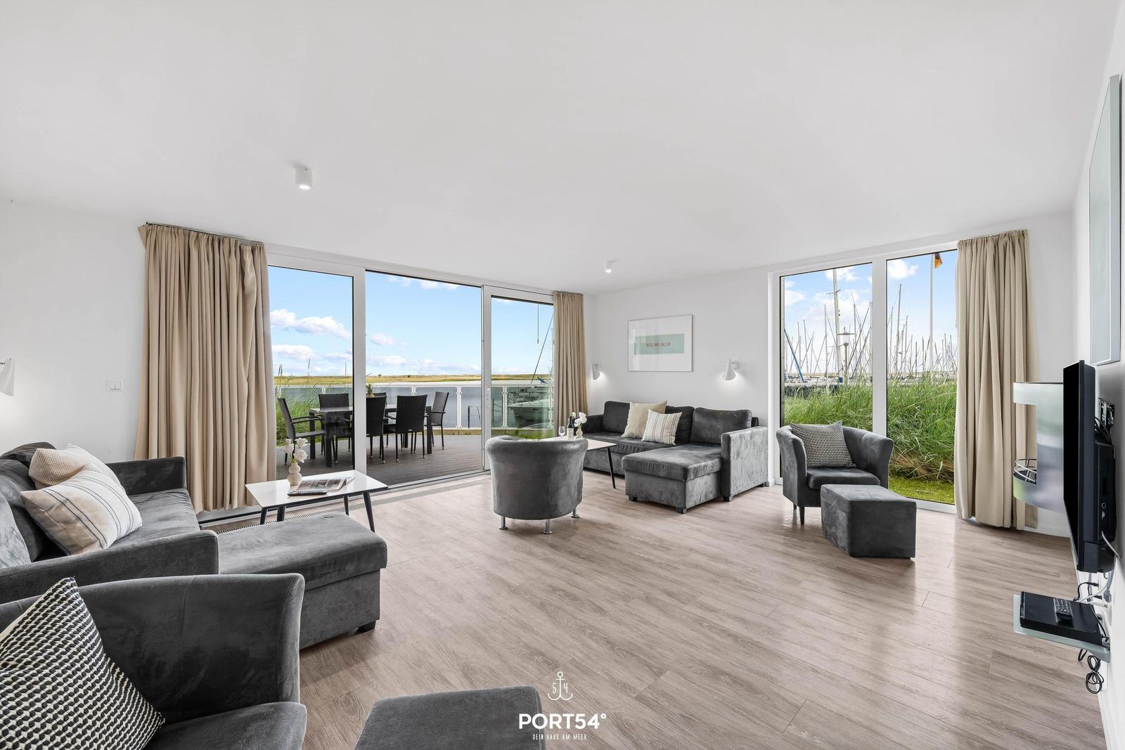 Wohnbereich mit grauen Sofas, Holzboden und großem Balkon mit Meerblick.