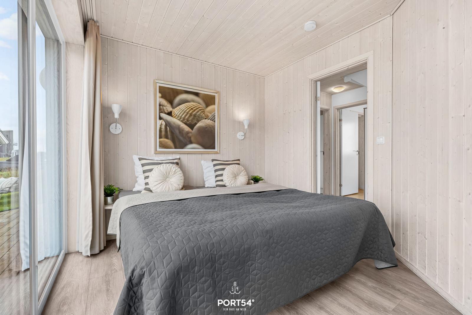 Schlafzimmer mit Bett, Wandbild und großem Fenster. Holzwand und -boden.