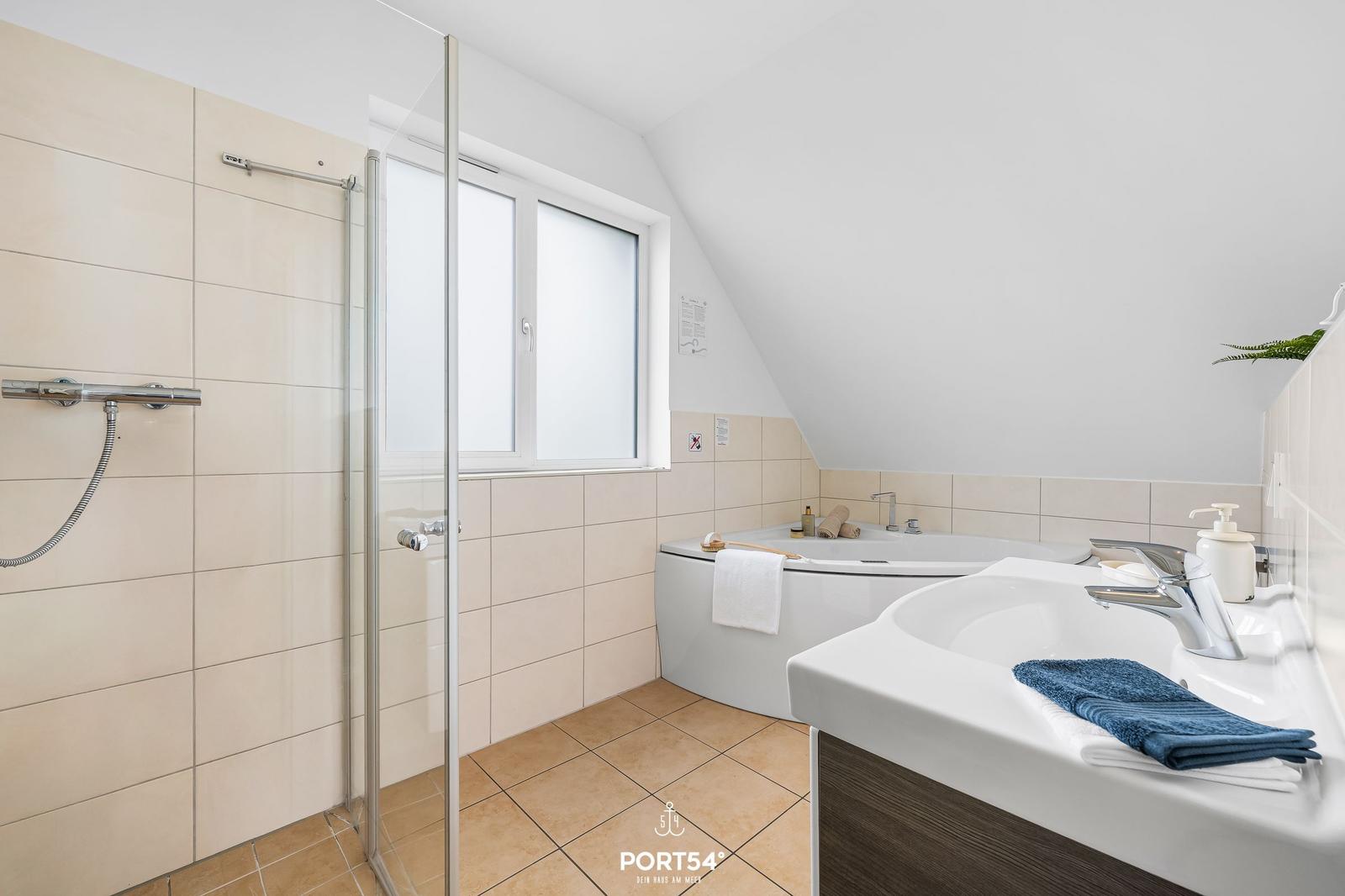 Badezimmer mit Dusche, Badewanne und Waschbecken. Fenster und Dachneigung sichtbar.