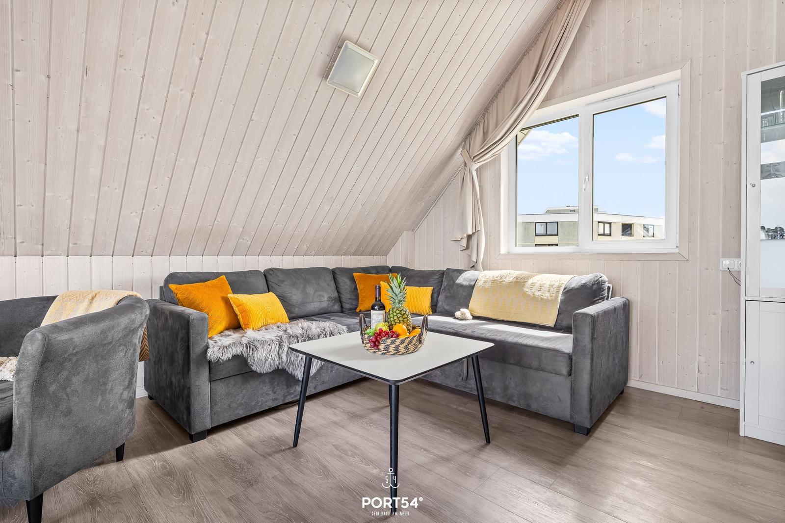 Wohnzimmer mit grauem Sofa, gelben Kissen und Holzwandverkleidung.