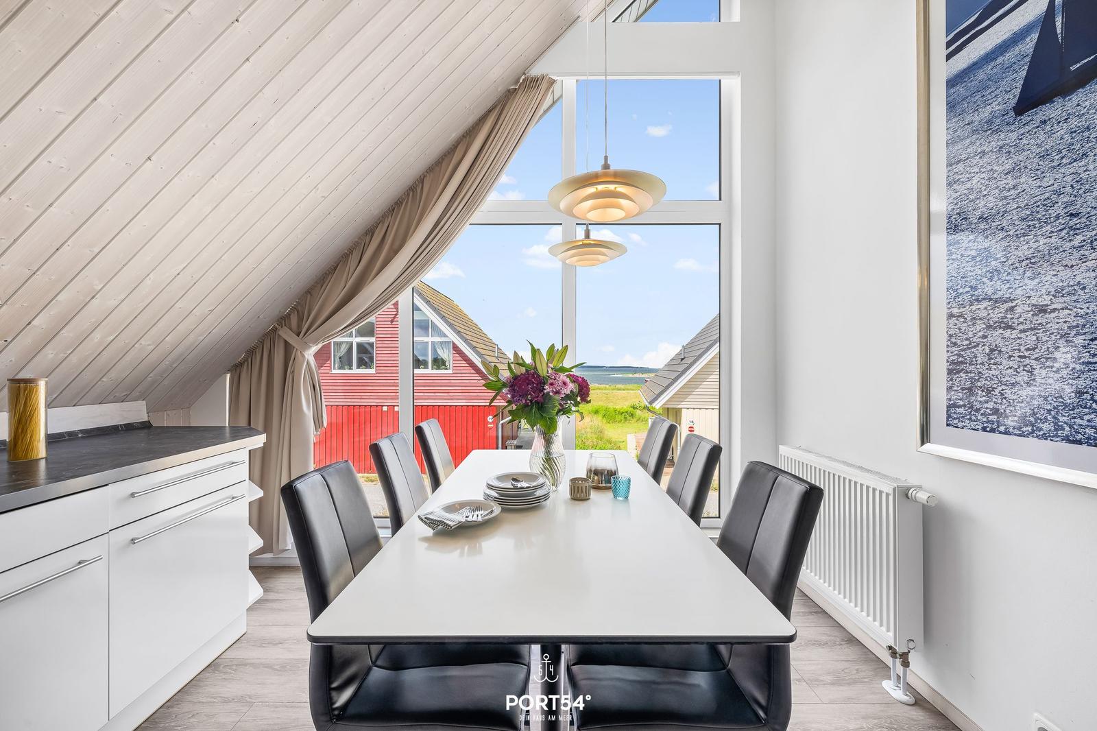 Essbereich mit weißem Tisch, schwarzen Stühlen und großem Fenster mit Blick auf rotes Haus.