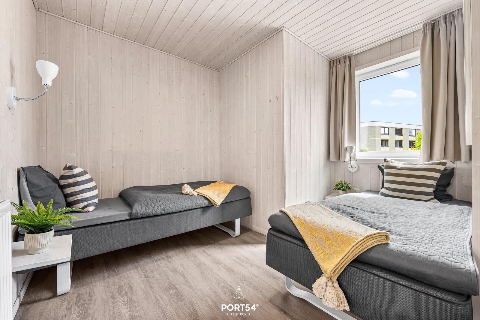 Zwei Schlafplätze mit Matratzen, Fenster und Holzwand. Zimmer mit Pflanzen und Lampen.