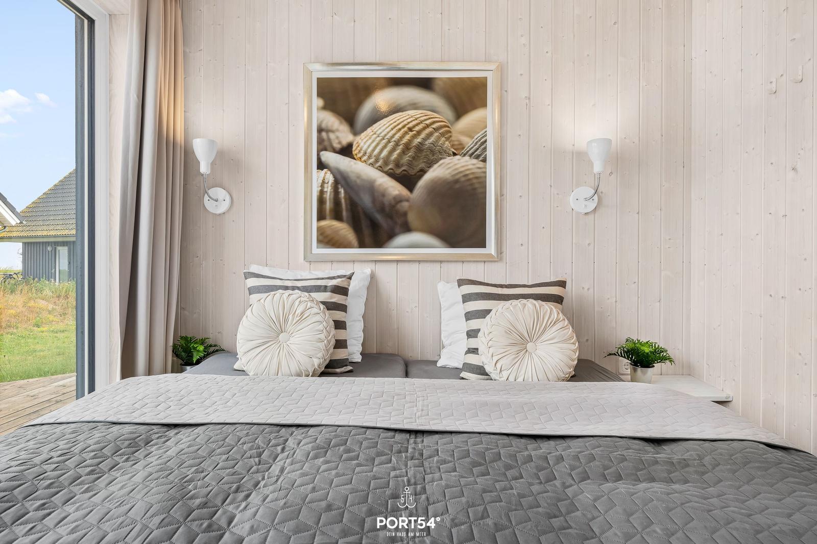Schlafzimmer mit Bett, Wandbild und Fensterblick auf Grünfläche.