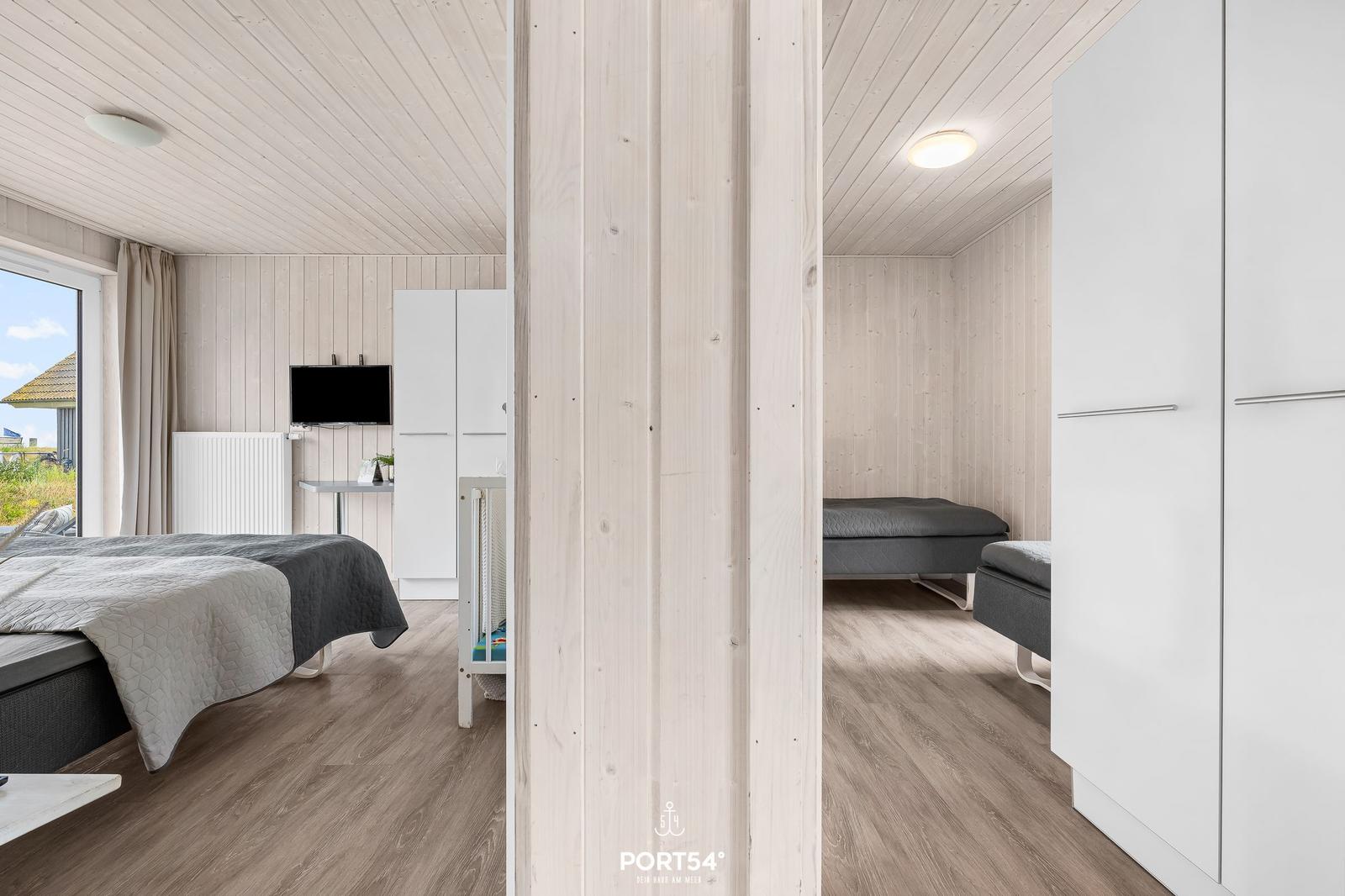 Schlafzimmer mit Bett, TV und Fenster. Nebenraum mit Schlafcouch und Kleiderschrank.