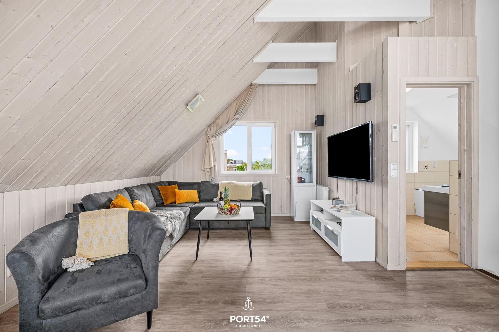 Wohnzimmer mit Sofa, Couch und Fernseher. Holzdecke und Boden. Blick in die Badewanne.