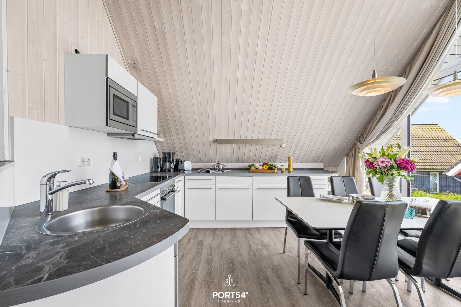 Küche mit Esstisch, schwarzer Arbeitsplatte und Holzdecke.