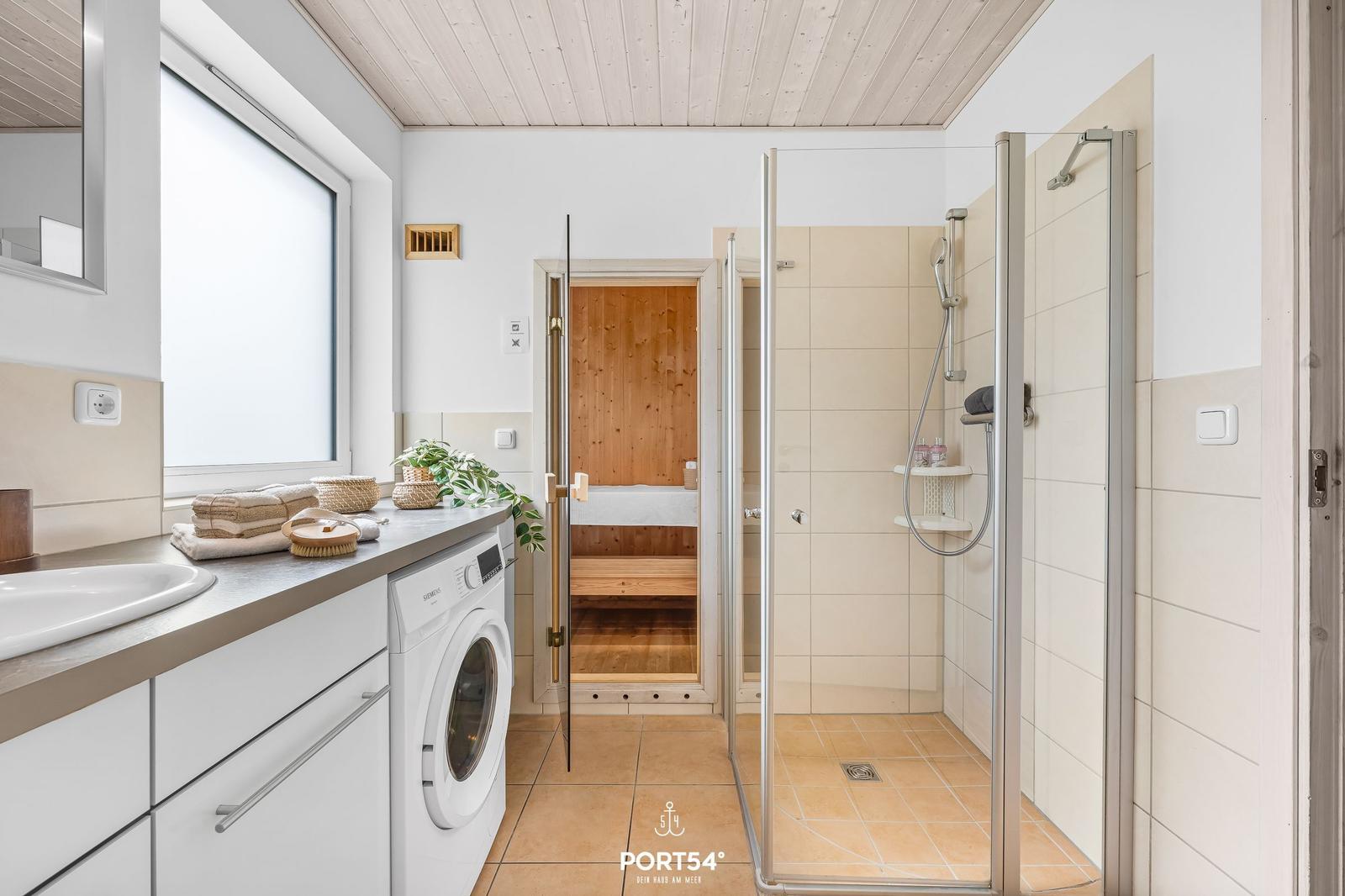 Bad mit Dusche, Waschmaschine und Sauna im Hintergrund.
