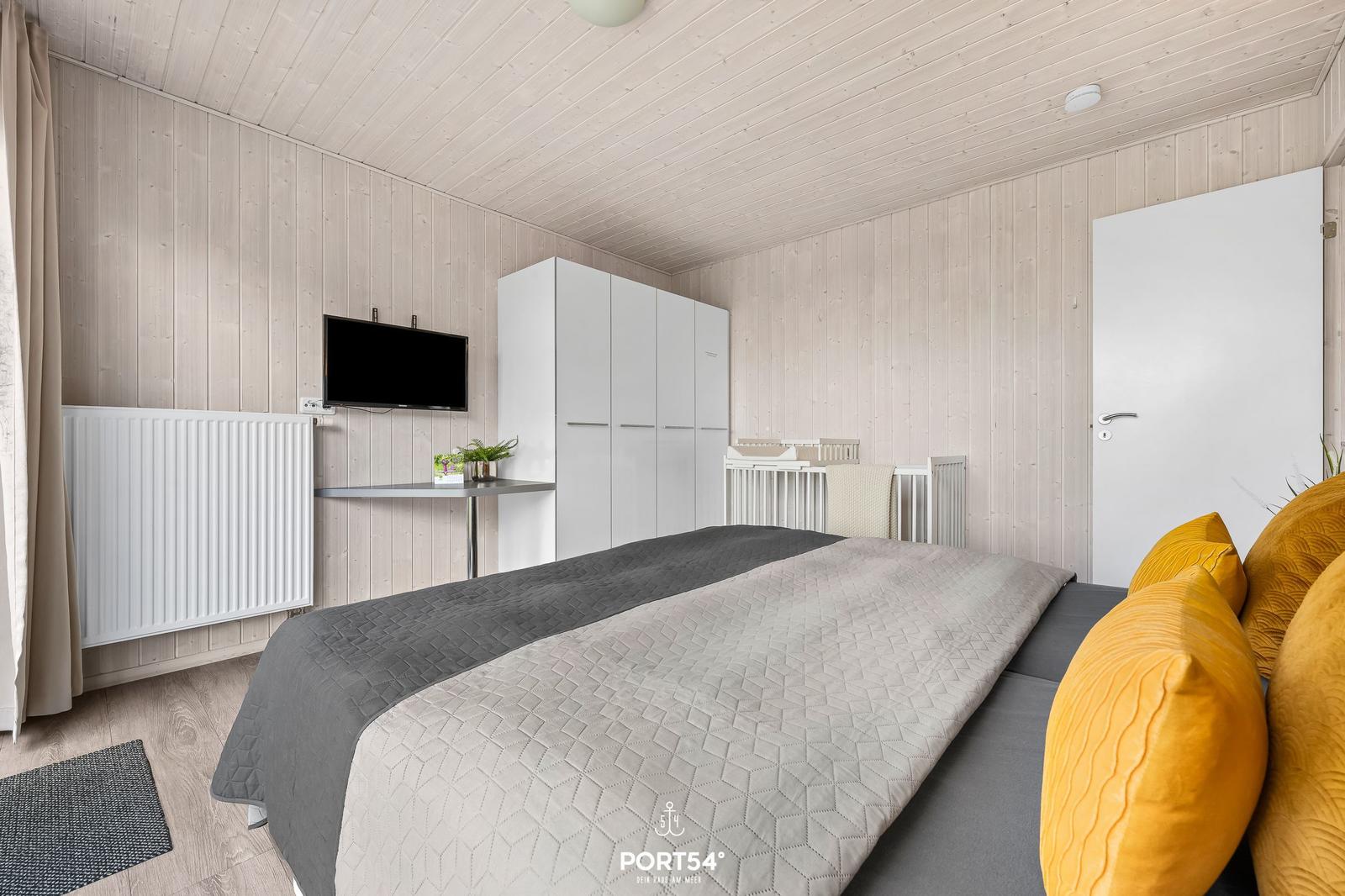 Schlafzimmer mit Bett, Kleiderschrank, TV und Babybett.