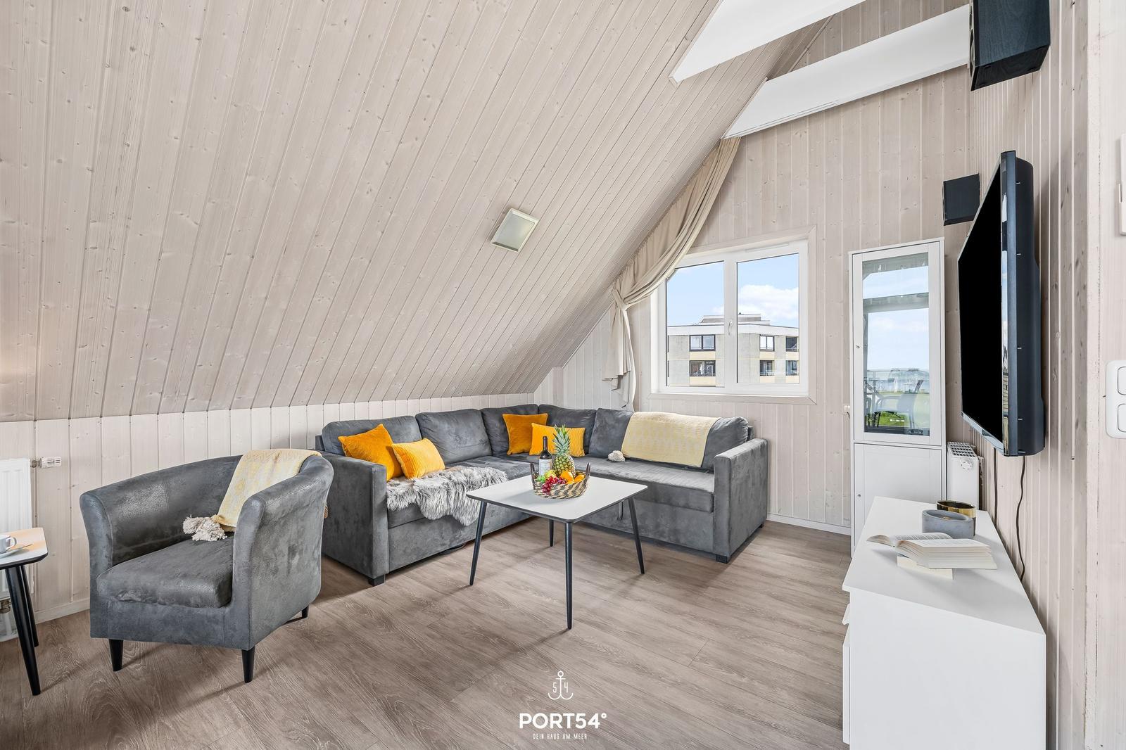 Wohnzimmer mit grauem Sofa, gelben Kissen und Holzfußboden unter schrägem Dach.