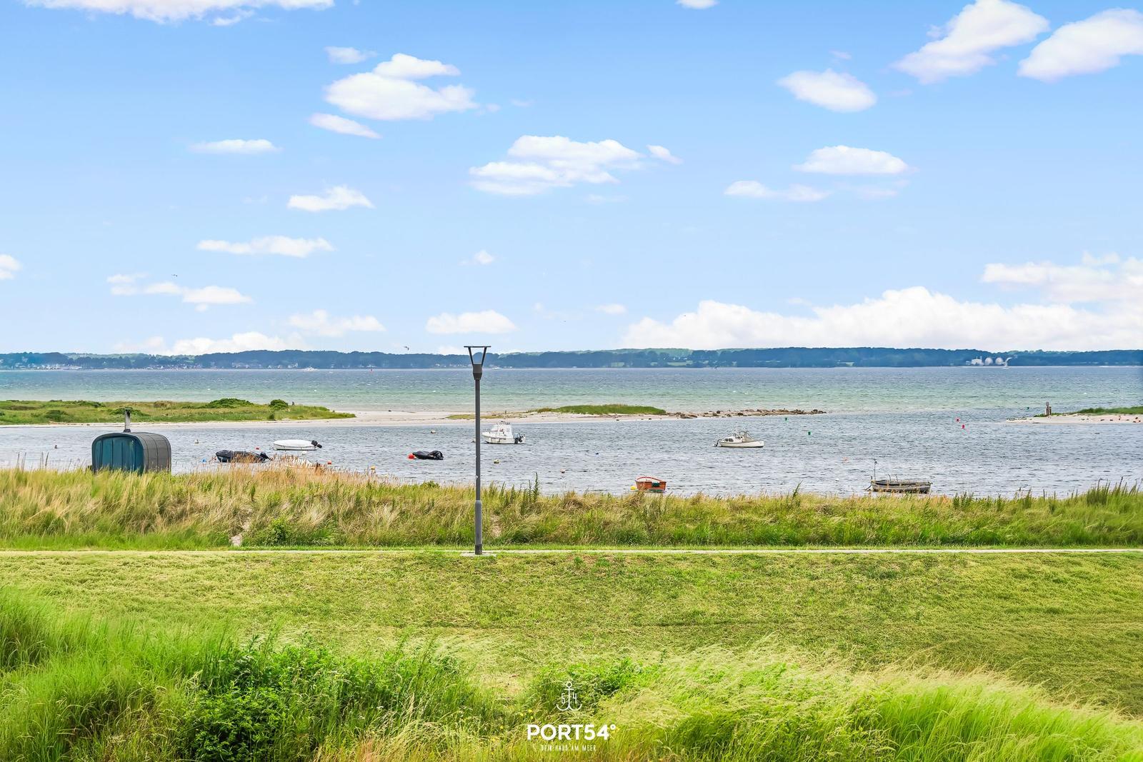 Grünes Grasfeld mit Blick auf das Meer und Boote.