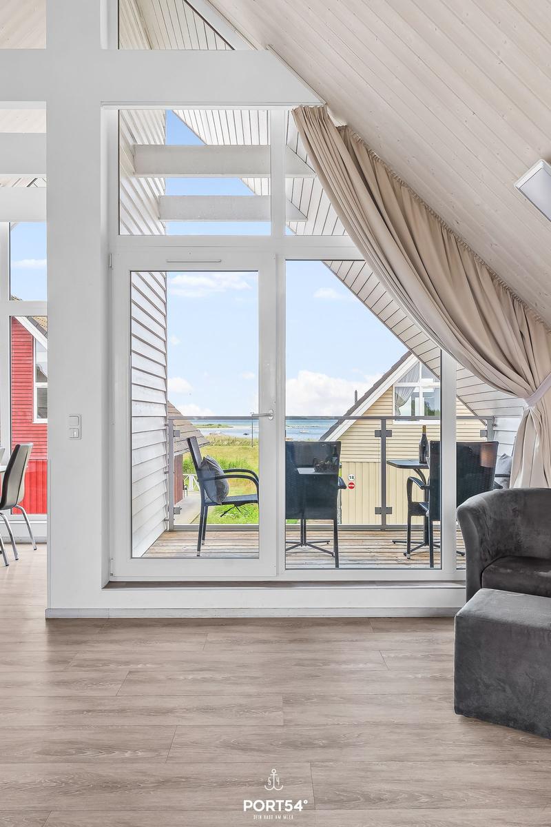 Durch große Fenster Blick auf Balkon mit Tisch und Stühlen sowie Meeresblick.