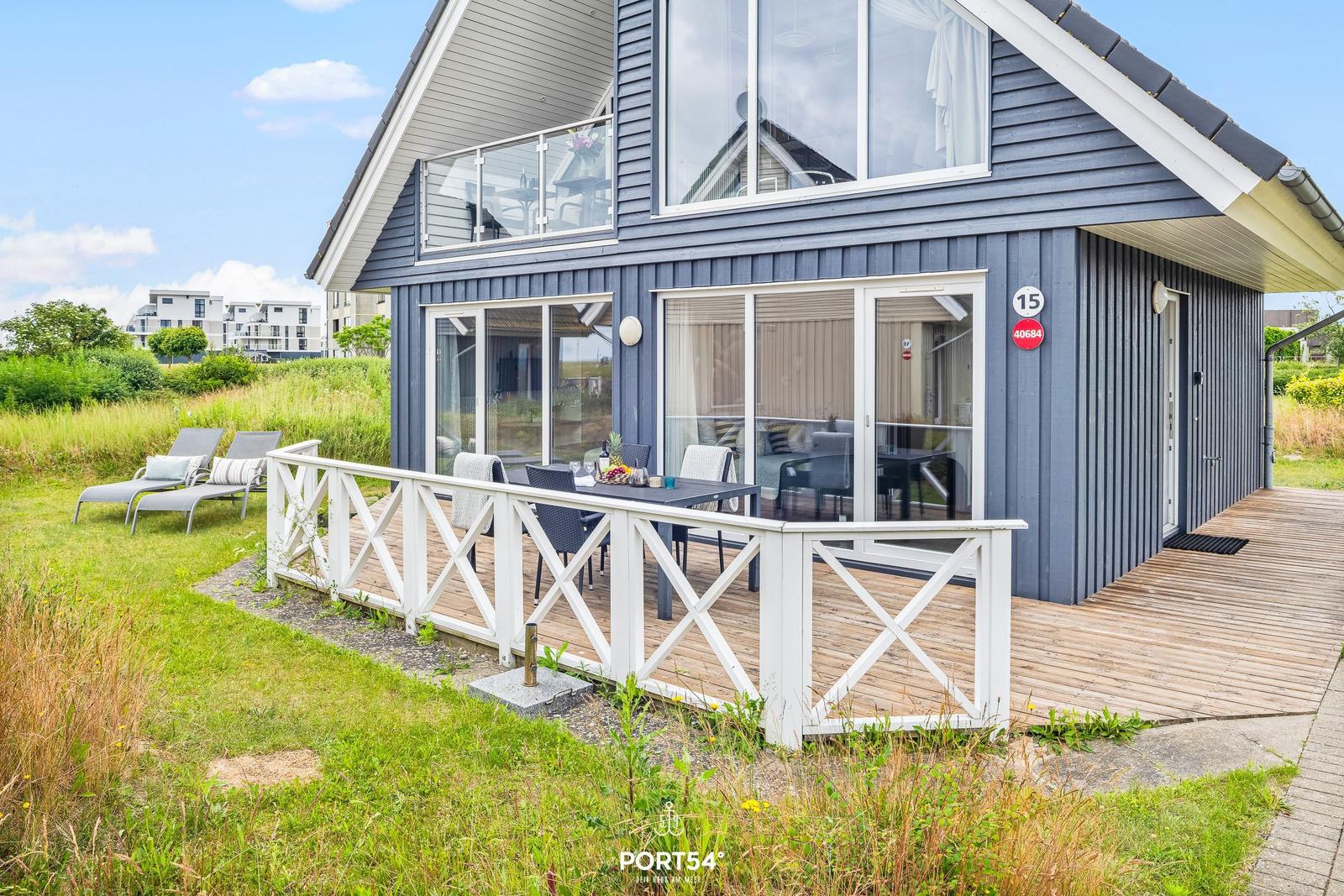 Haus mit Terrasse, Gartenliegen und großem Fensterbereich. Hausnummer 15.
