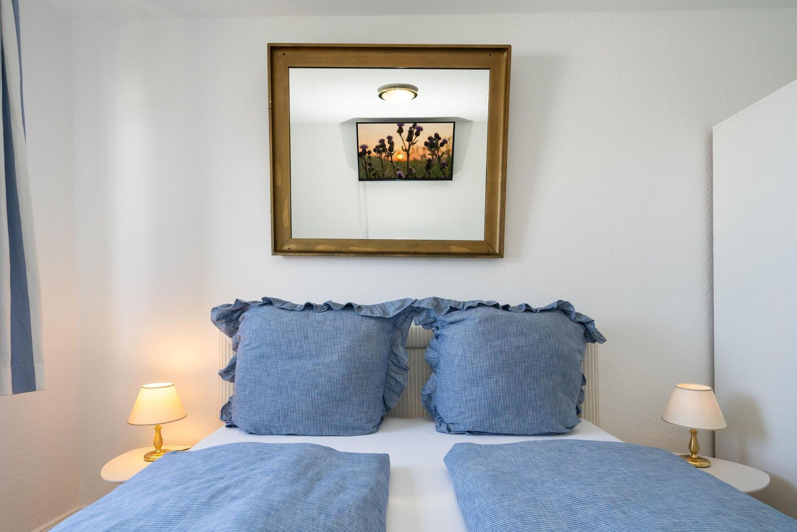 Ein Bett mit blauen Kissen und Bettwäsche, zwei Nachttische mit Lampen und ein Spiegel an der Wand.
