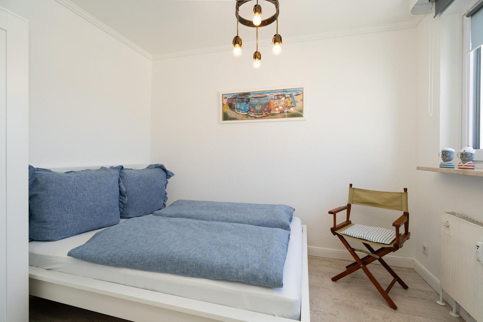 Schlafzimmer mit Bett, Stuhl und Wandbild.