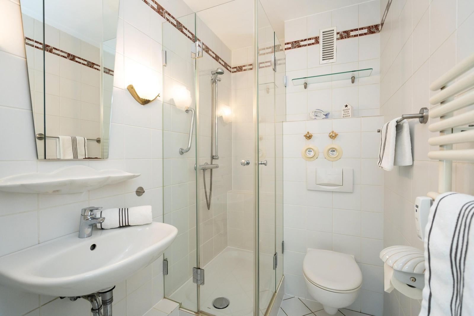 Badezimmer mit Dusche, Waschbecken und Toilette. Weiße Fliesen und Glaswand.