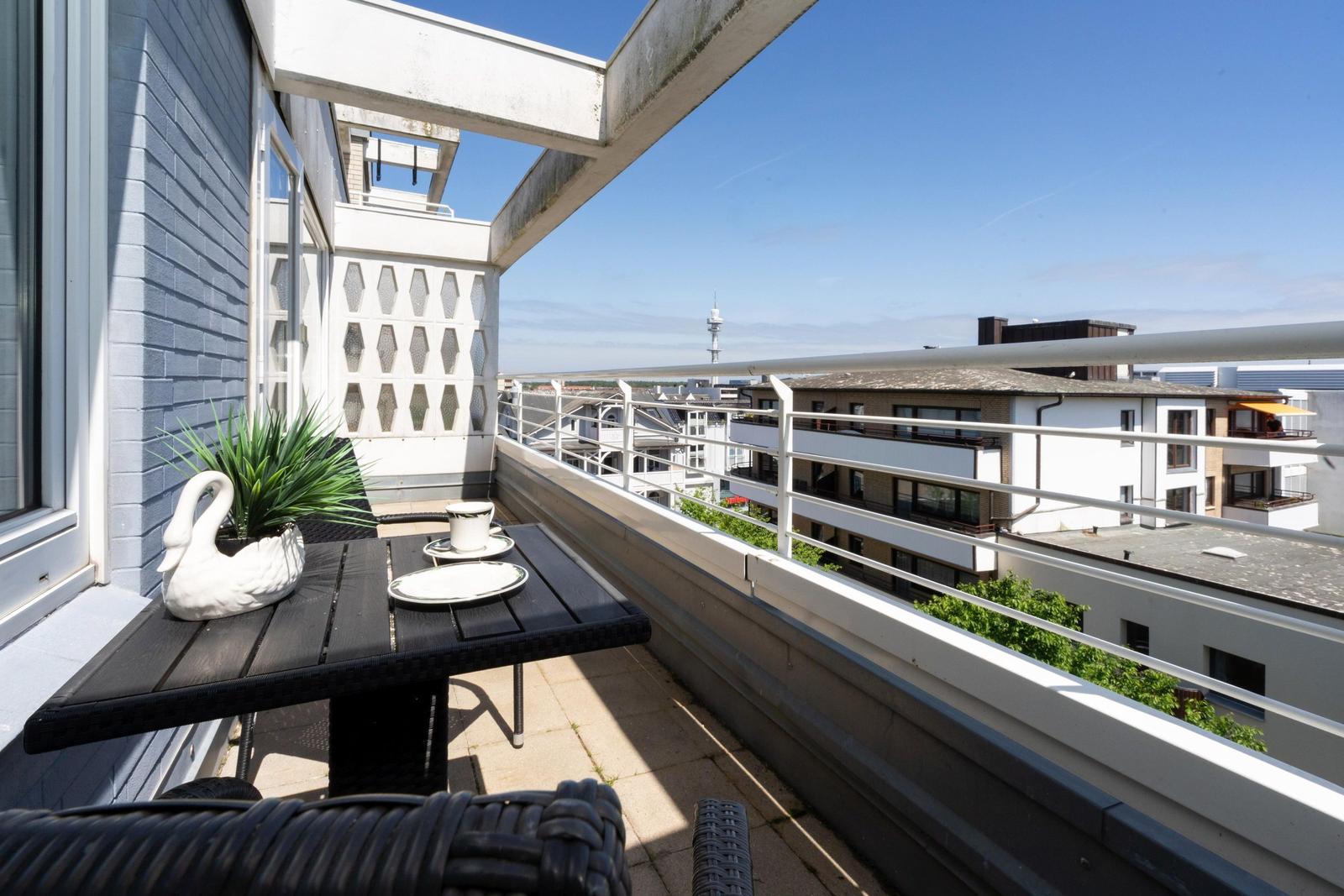 Terrasse mit Tisch, Stühlen und Pflanze. Blick auf Wohngebäude und Fernsehturm.