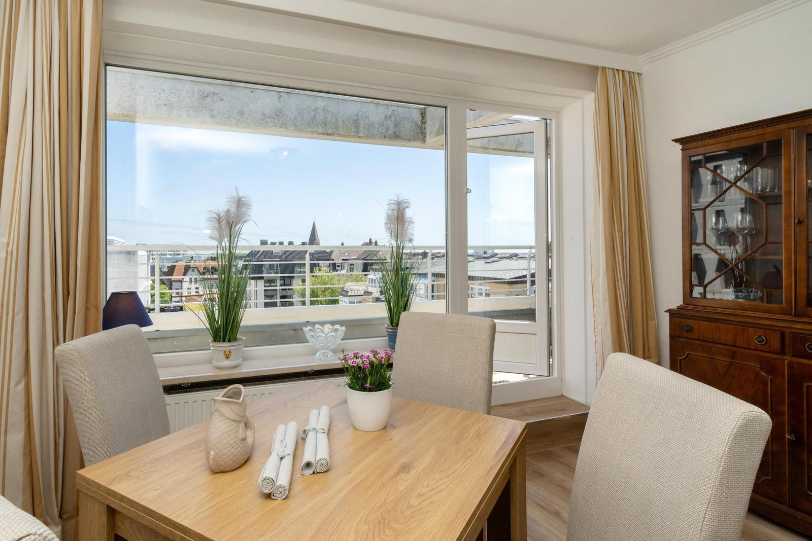 Esszimmer mit Tisch, Stühlen und Blick auf Balkon. Holztisch, Beistelltisch und Gardinen.